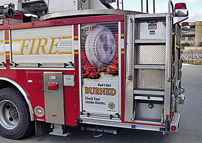 A billboard on a London fire truck that depicts flames surrounding a smoke alarm that has been tampered with reads ‘Don’t get burned. Check your smoke alarms.’