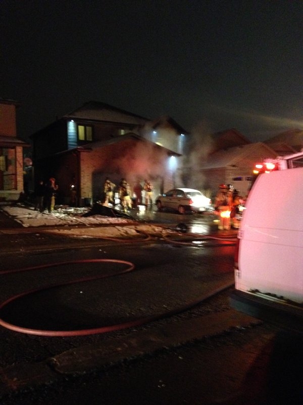 Fire crews in smoke working at the front of a two car garage home