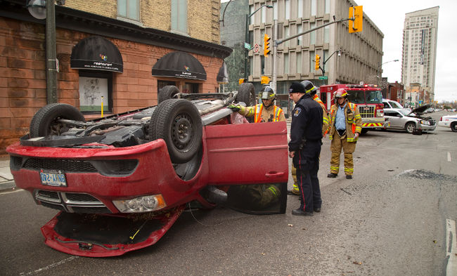 Const. Antoni Uchmanowicz talks to firefighters at the scene of a Sunday morning rollover at King and Richmond streets in London. Mike Hensen/The London Free Press/Postmedia Network