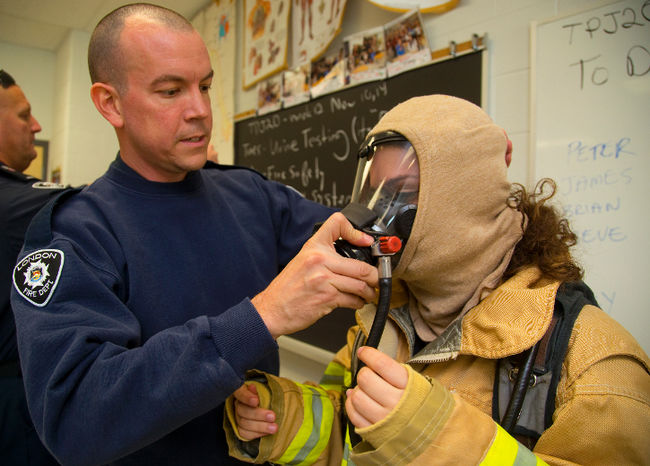 London firefighter James Bell helps student volunteer Jennifer Eid, 15 of Saint André Bessette Catholic Secondary School into their bunker gear including breathing apparatus during a Health Technology class at the school in London, Ont. on Monday November 10, 2014. Mike Hensen/The London Free Press/QMI Agency