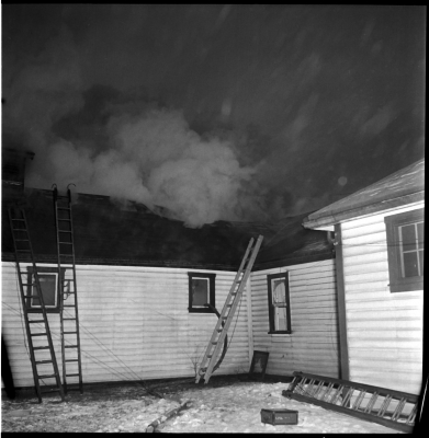Several ladders propped up against a wood sided building.