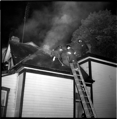 Three fire fighters on a roof extinguishing fire in the roof and attic