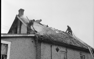 Fire fighters on roof ladders accessign attic to extinguish hot spots