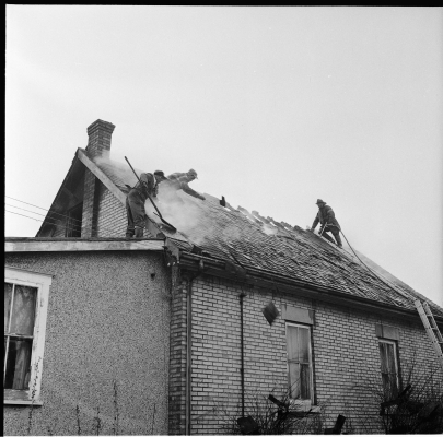 Fire fighters on roof ladders accessign attic to extinguish hot spots