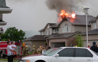 Garage roof on fire, fire fighters gathering to attack garage roof fire.