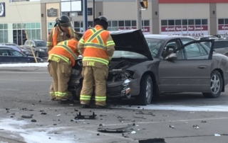 Two fire fighters looking at engine of vehicle involved in crash.