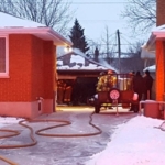 Hose stretches up a driveway to an extinguished garage fire