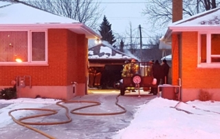 Hose stretches up a driveway to an extinguished garage fire