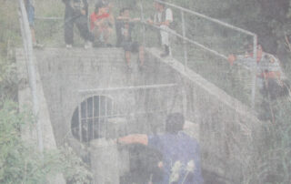 Firefighters and on-lookers looking into a storm sewer