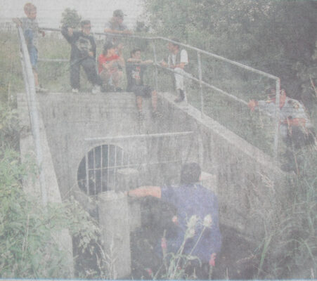 Firefighters and on-lookers looking into a storm sewer