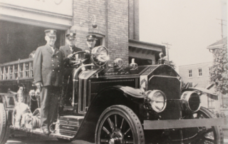 Three London Fire Fighters pose on their fire apparatus in front of Station 5
