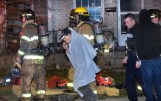Police officer and two fire fighters around a civilian wrapped in a blanket