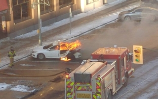 Fire fighters deploying to extinguish car engulfed in flames.