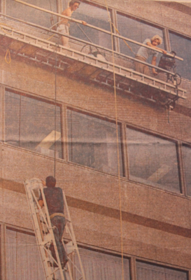 Two stranded window washers talking to a firefighter on a ladder approximately 110 feet on the side of a building.
