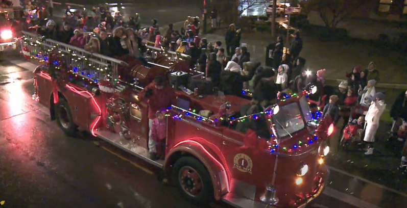 Vintage open cab fire truck with families waving at the parade crowds.