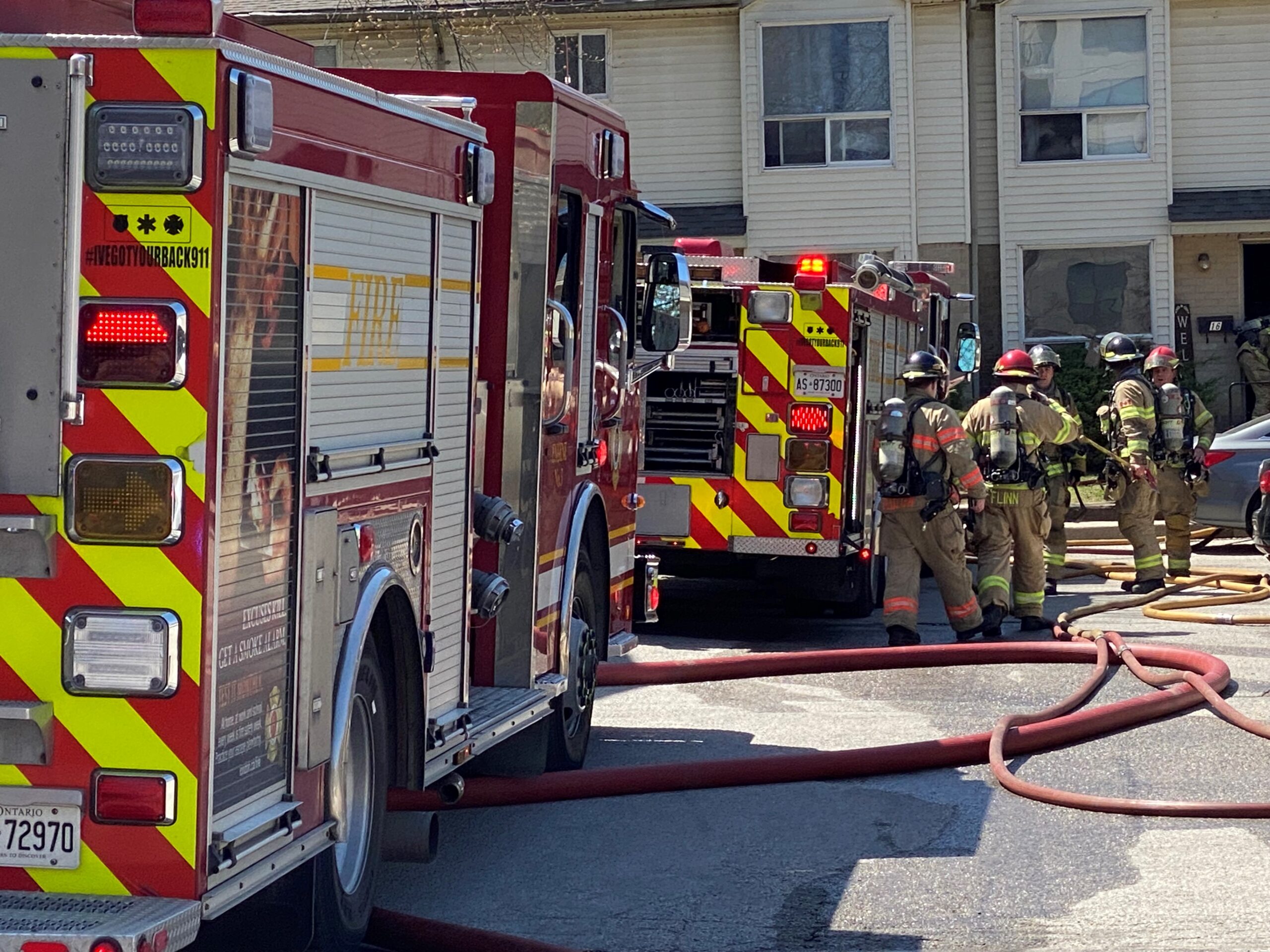 Fire trucks, personnel, and hoses in the parking lot area of a townhouse complex.