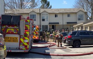Fire trucks, personnel, and hoses in the parking lot area of a townhouse complex.