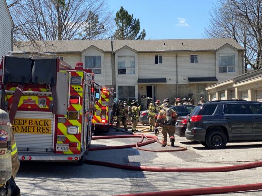 Fire trucks, personnel, and hoses in the parking lot area of a townhouse complex.