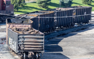 Six open-top railcars with burnt contents sitting in a rail yard