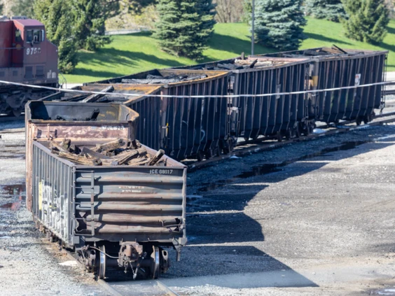Six open-top railcars with burnt contents sitting in a rail yard