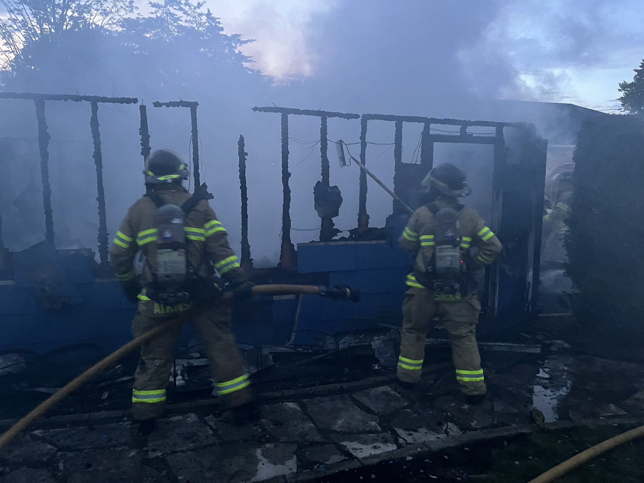 Two firefighters pulling apart the remains of a burnt out garage.