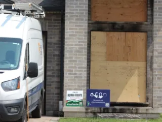 Renovation van in the driveway of a home with the front door boarded up with plywood.