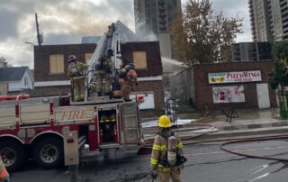 Large fire truck spary water from large ladder onto vacant two story building