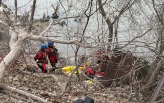 LFD Water Ice Rescue Team members at the rivers' edge working through debris and trees to gain access to the patient in the waer