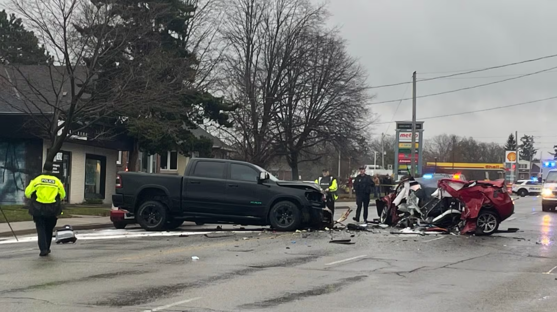 Serious crash sends two people to hospital A black pickup truck and a severely damaged red car sit across Adelaide Street North after a major collision, with debris scattered over the roadway. Police officers and emergency responders stand near the wreckage while patrol vehicles block the road and emergency lights flash in the background.