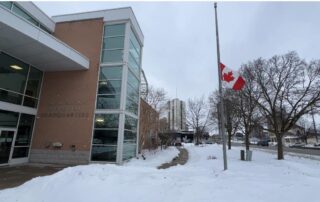 Canadian flag at half-mast outside London Fire Department Memorial Headquarters on a snowy winter day, recognizing those affected by the tragedy in Tumbler Ridge, British Columbia.